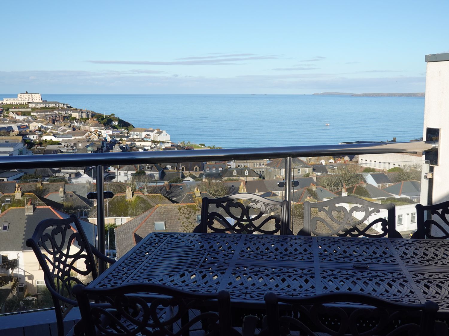 A balcony with a metal table and chairs overlooking a town and the ocean at 2 Quay Court in Newquay