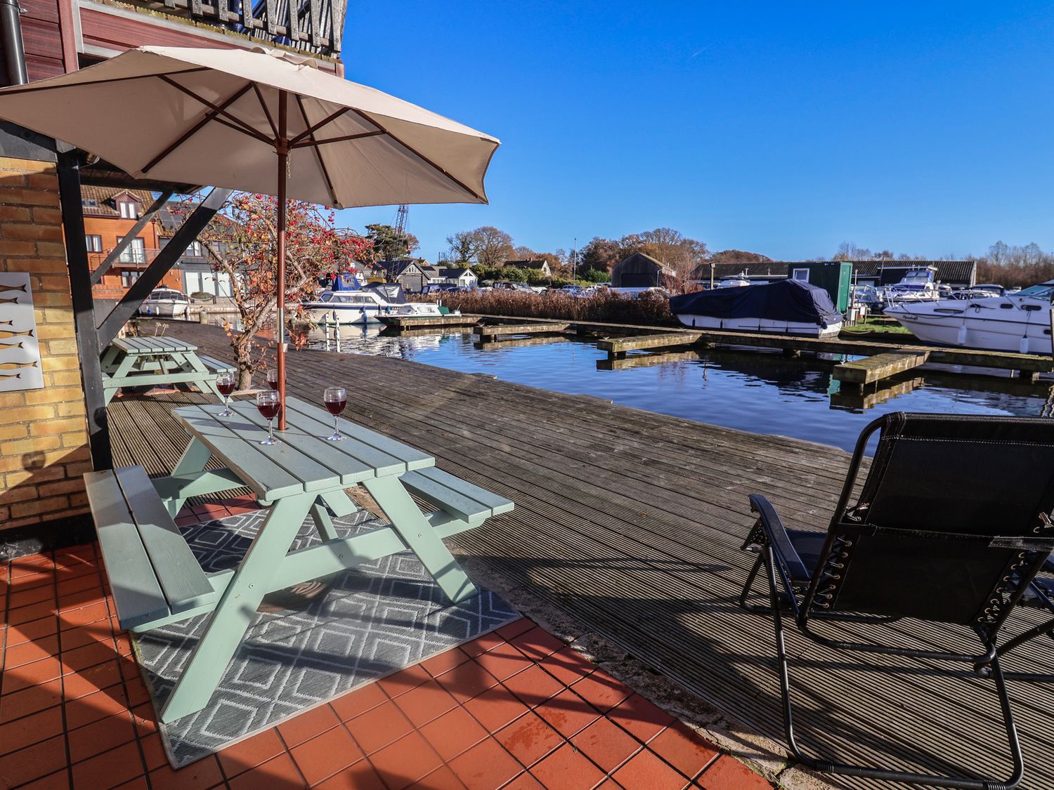 An outdoor seating area by the water with boats at Daisy Lodge in Norwich
