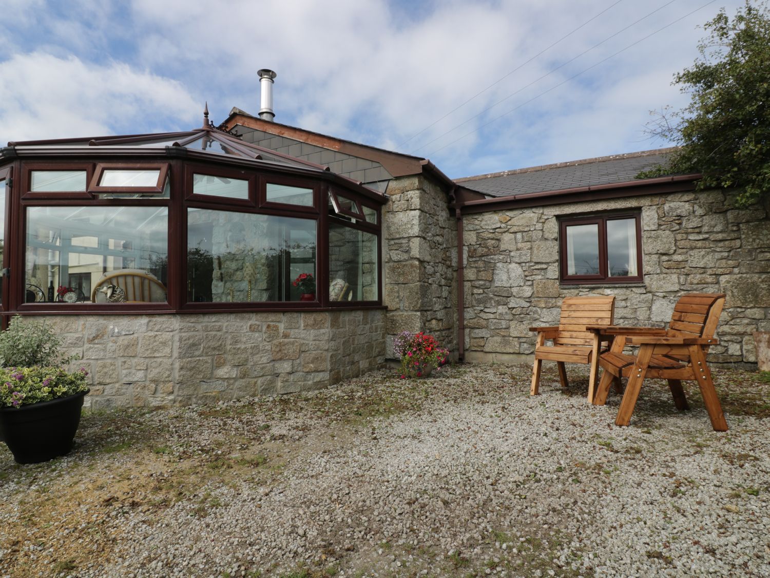 A stone building with a conservatory and wooden chairs outside at Sheilas Cottage in Penryn