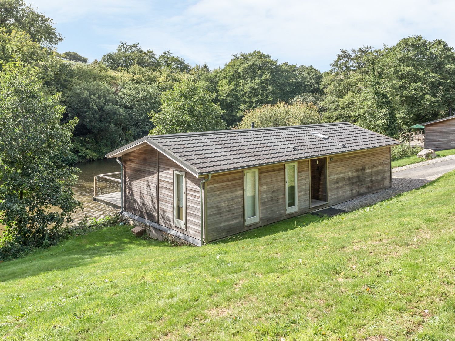 A wooden house with a tiled roof on a grassy slope near trees and a river at 7 Water's Edge in Lanreath