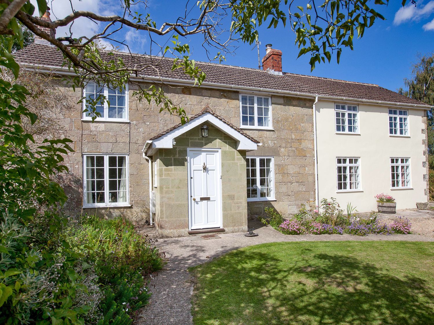 A stone and plaster house with a white door and multiple windows in a garden at Church View in Salisbury