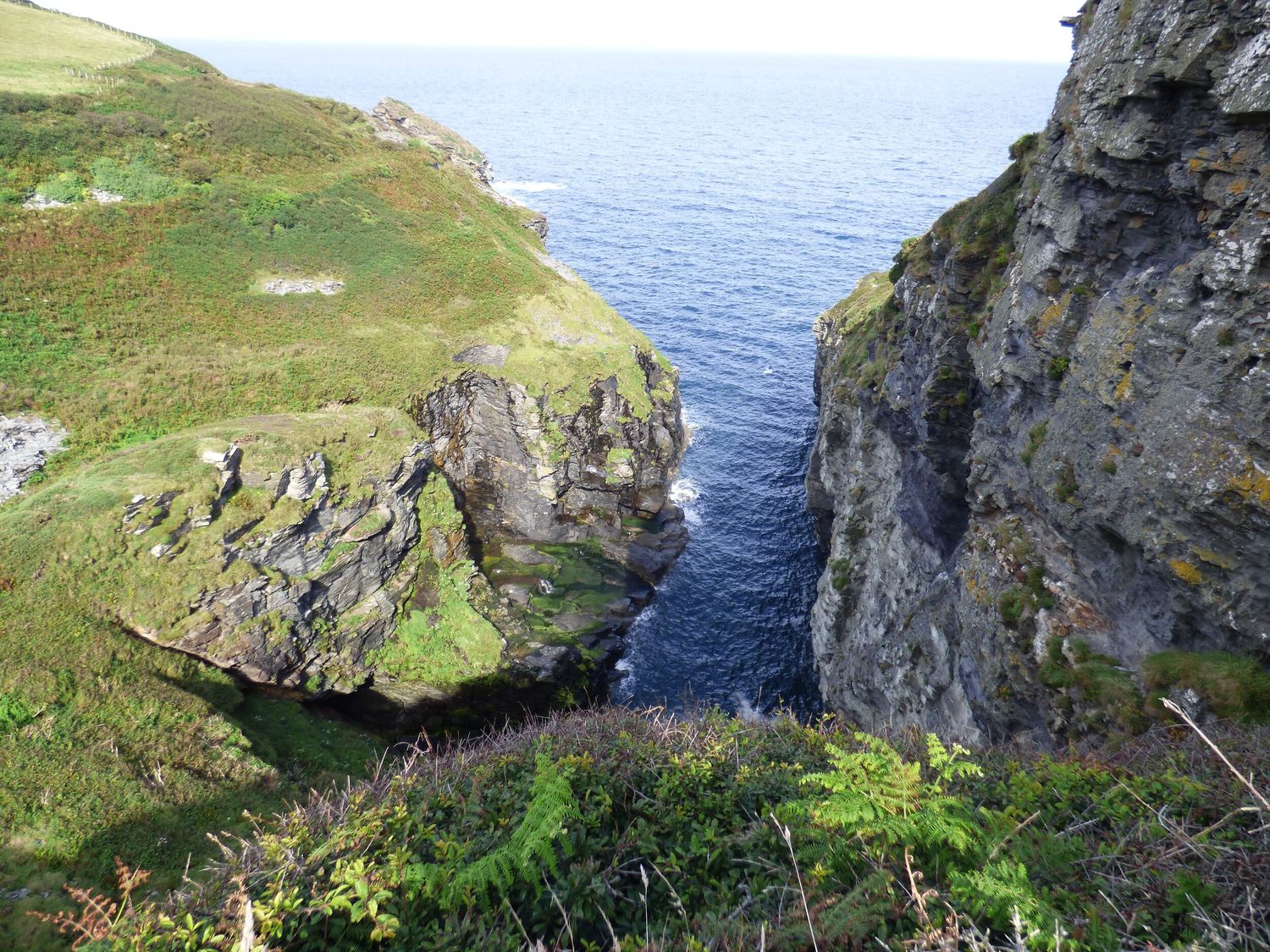 A coastal cliff with green grass and rocky formations overlooking the sea at Coastal Haven in Crackington near Crackington Haven