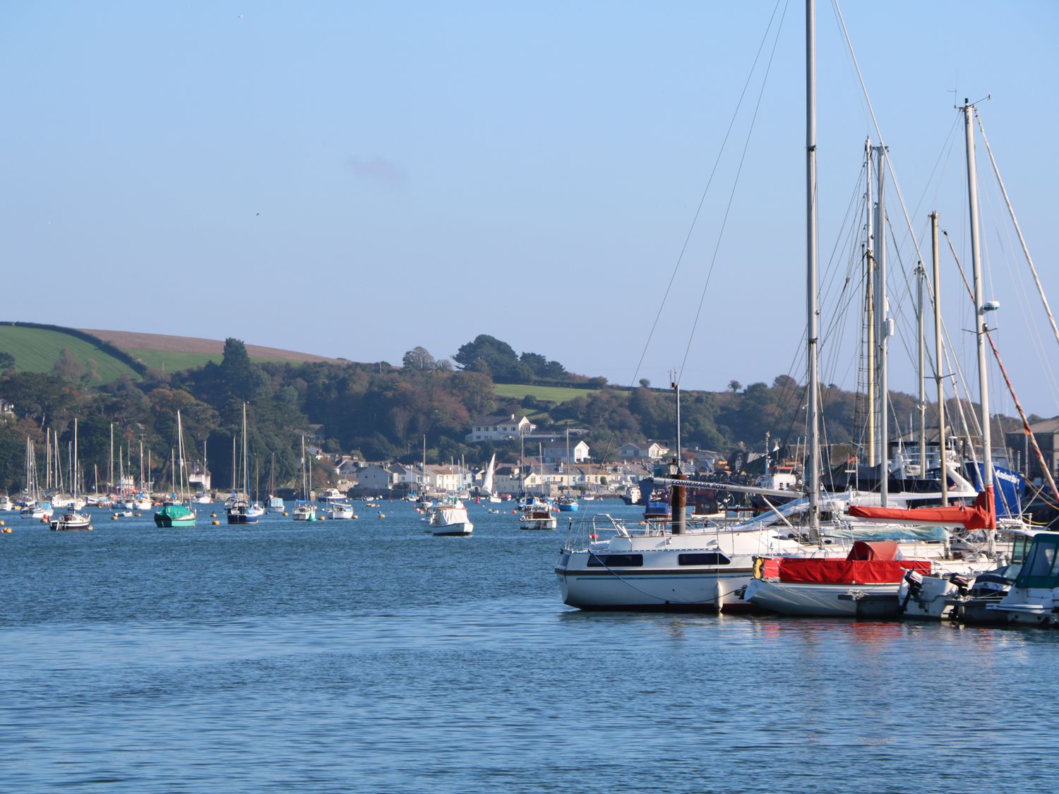 A harbor with sailboats and motorboats on water with hills and buildings in the background at Phenests in Falmouth