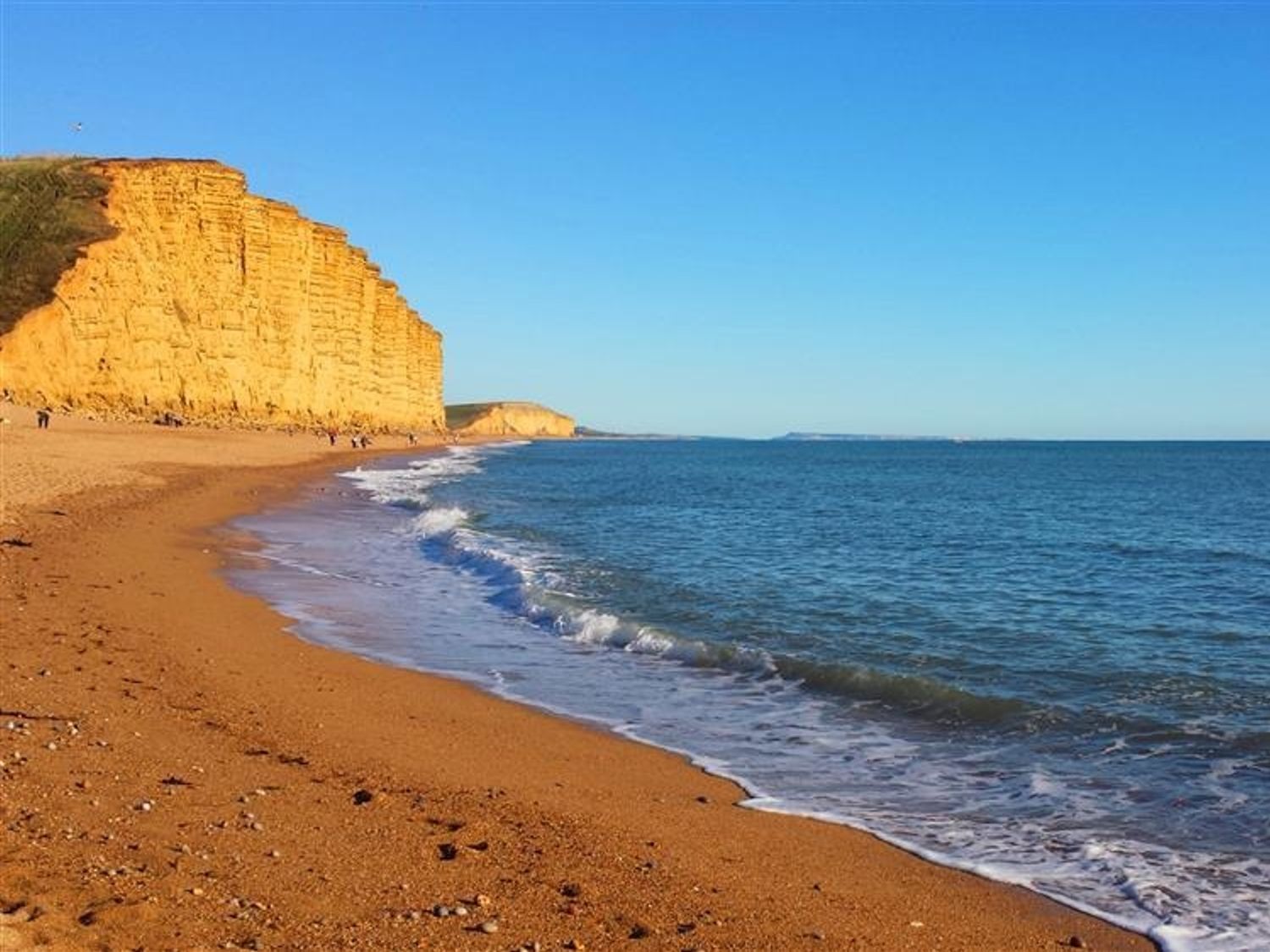A beach with sand and waves and a large cliff in the background at The Boardwalk in West Bay