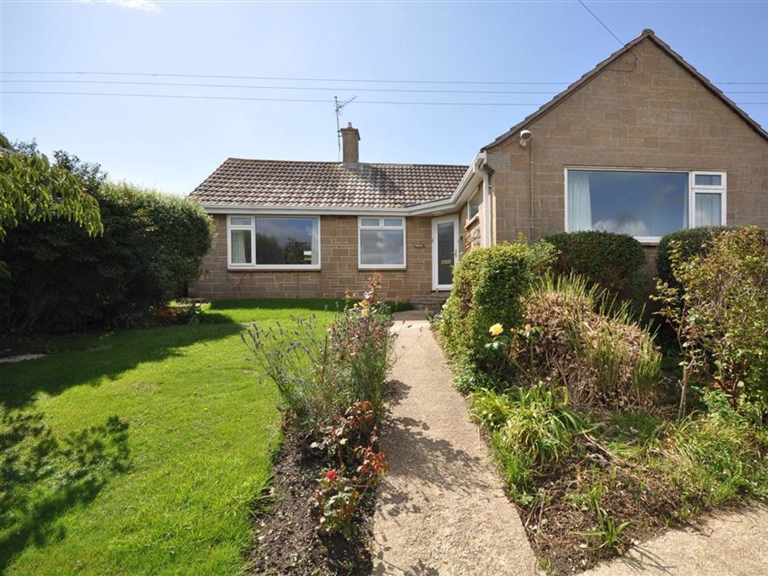 A single story house with a tiled roof and garden with a pathway at Pebbles in Burton Bradstock