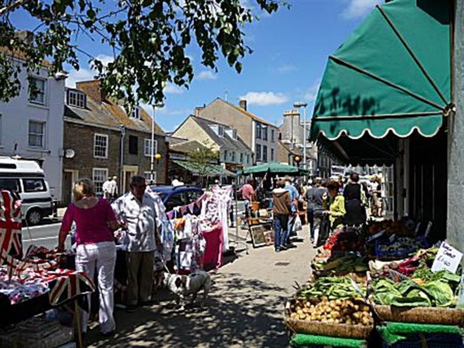 A street market with stalls selling vegetables clothing and other items and people walking at Pebbles in Burton Bradstock