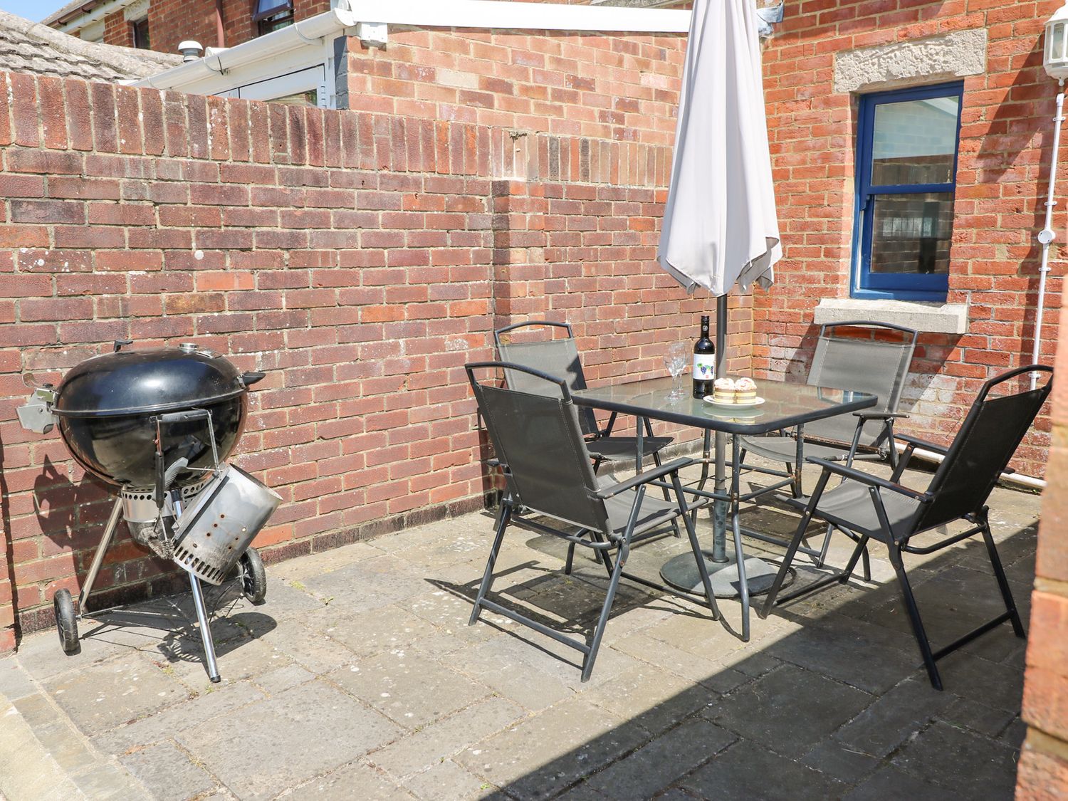 An outdoor patio with a barbecue grill a glass table with an umbrella and four chairs at Studland Cottage in Studland