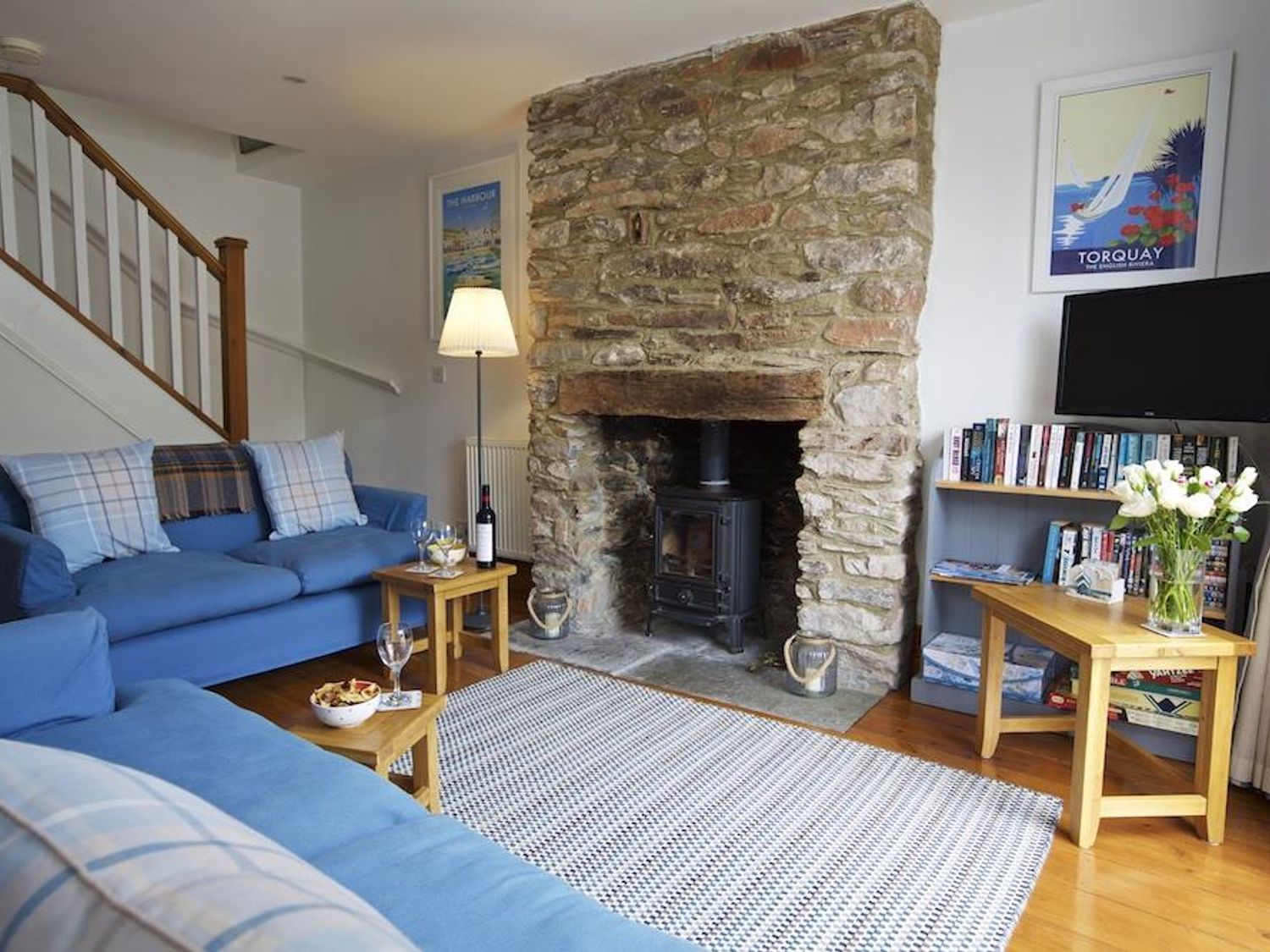 A living room with blue sofas a stone fireplace a wooden floor and shelves filled with books at Armada Cottage in Dartmouth