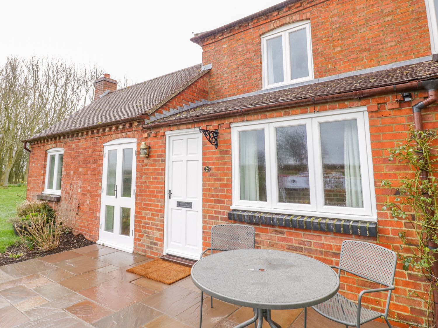 A patio with a round metal table and two chairs outside a red brick house at Wigrams Canalside Cottage in Napton-on-the-Hill