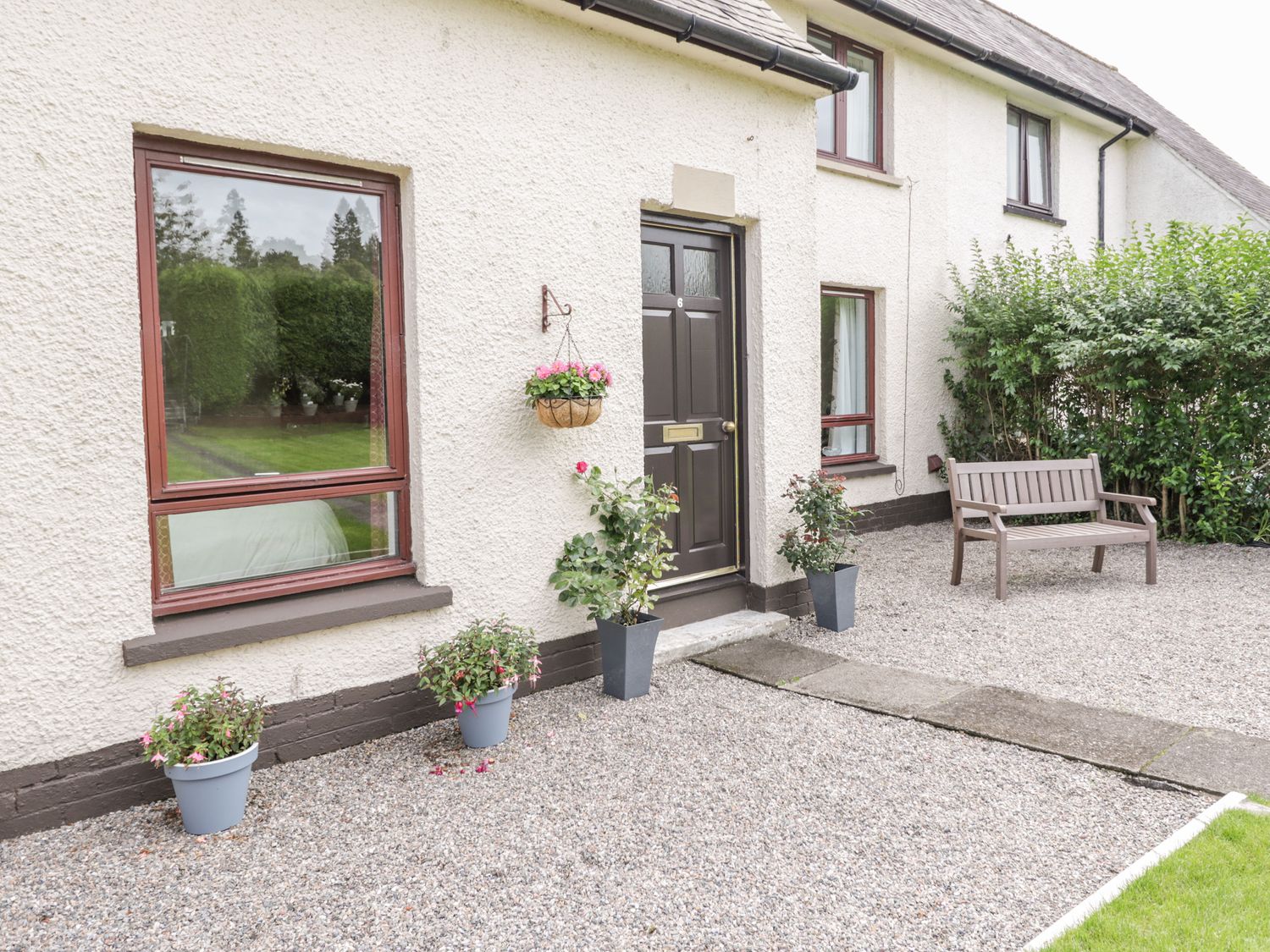 The exterior of a house with a black front door surrounded by plants in pots and a wooden bench on a gravel area at 6 Aonachan Gardens in Spean Bridge near Fort William