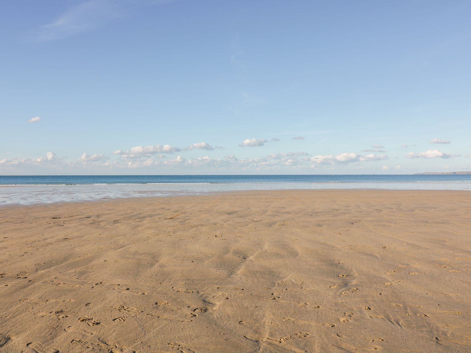 A sandy beach with footprints leading to the ocean under a blue sky at Apartment no.21 in Newquay