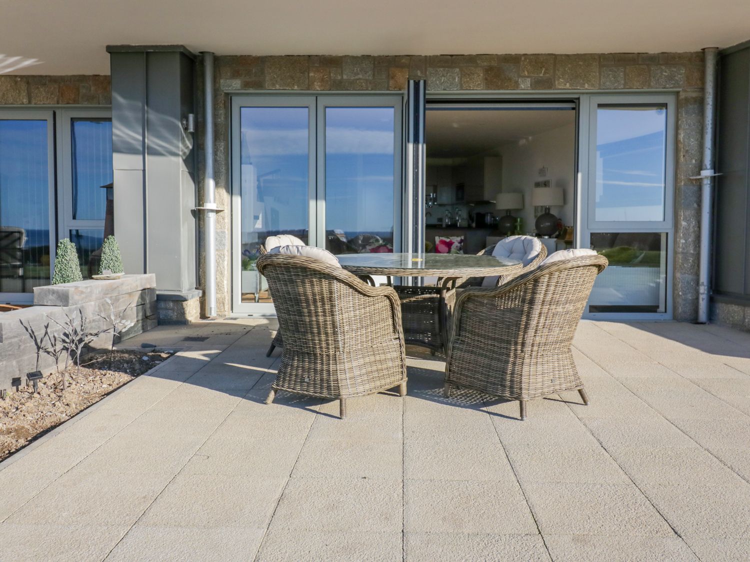 An outdoor patio with a round table and four wicker chairs in front of glass doors at Apartment no Twentyone in Newquay