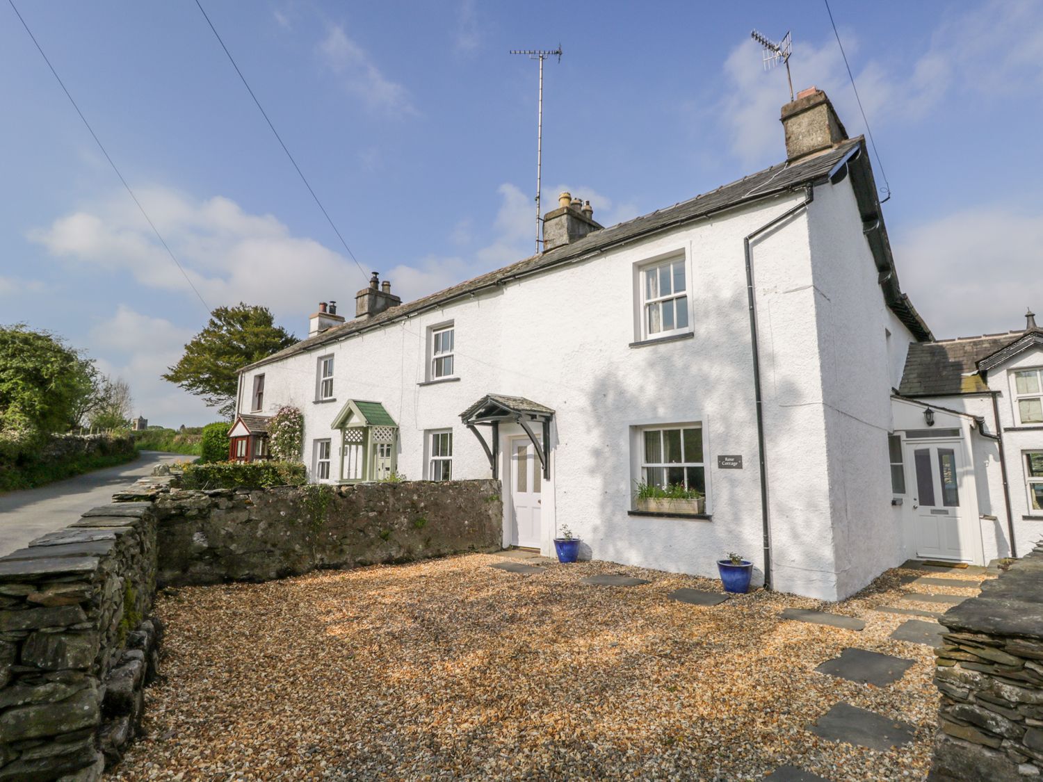 A white cottage with gravel driveway and stone wall at Rose Cottage Lowick Bridge