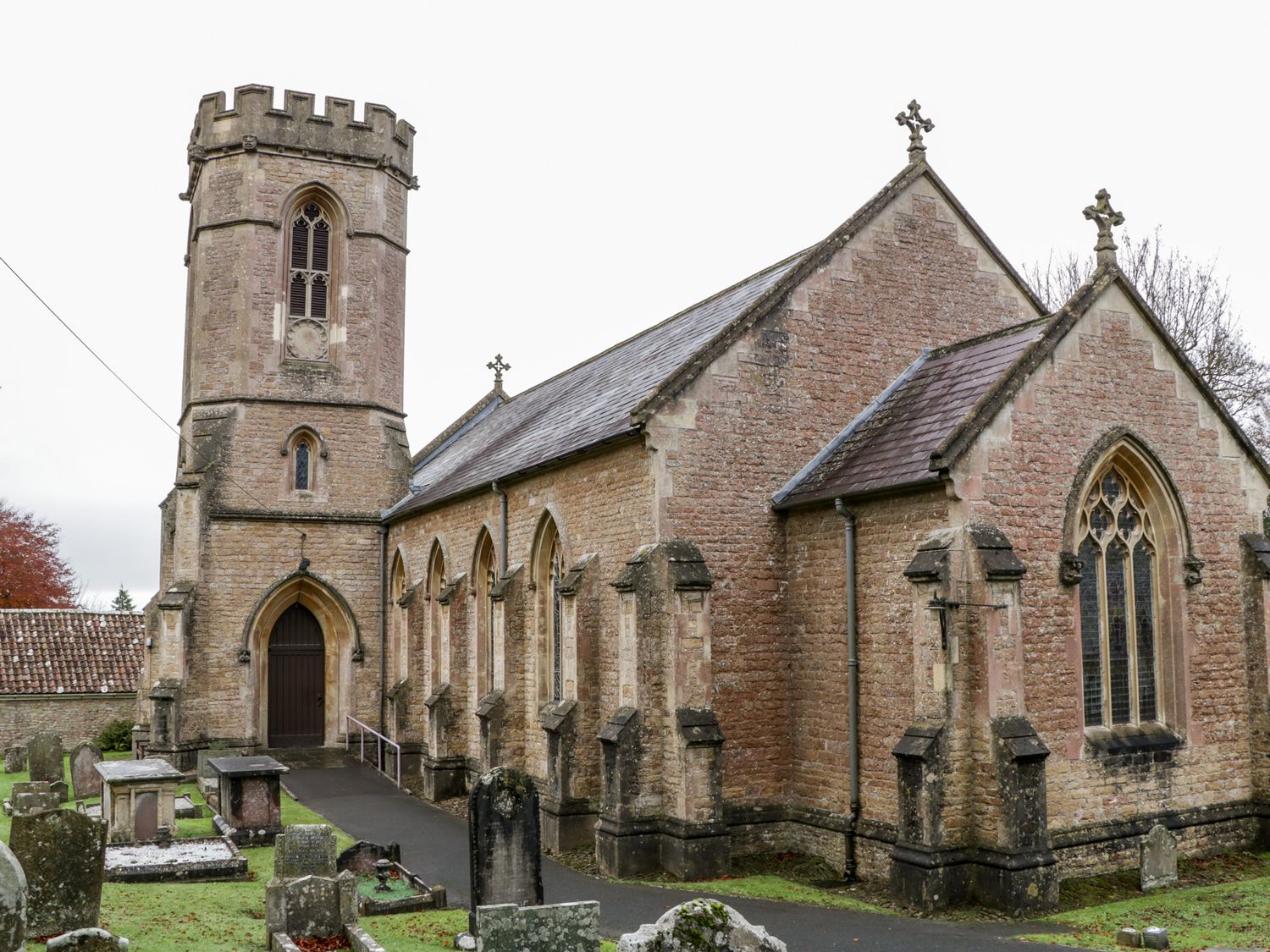 An old stone church with a tower and arched windows surrounded by gravestones at Stable Cottage in Shipham