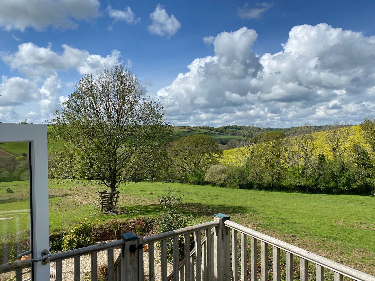 A countryside view with a wooden railing in the foreground and trees and fields under a partly cloudy sky at Ribby Farmhouse in Lerryn