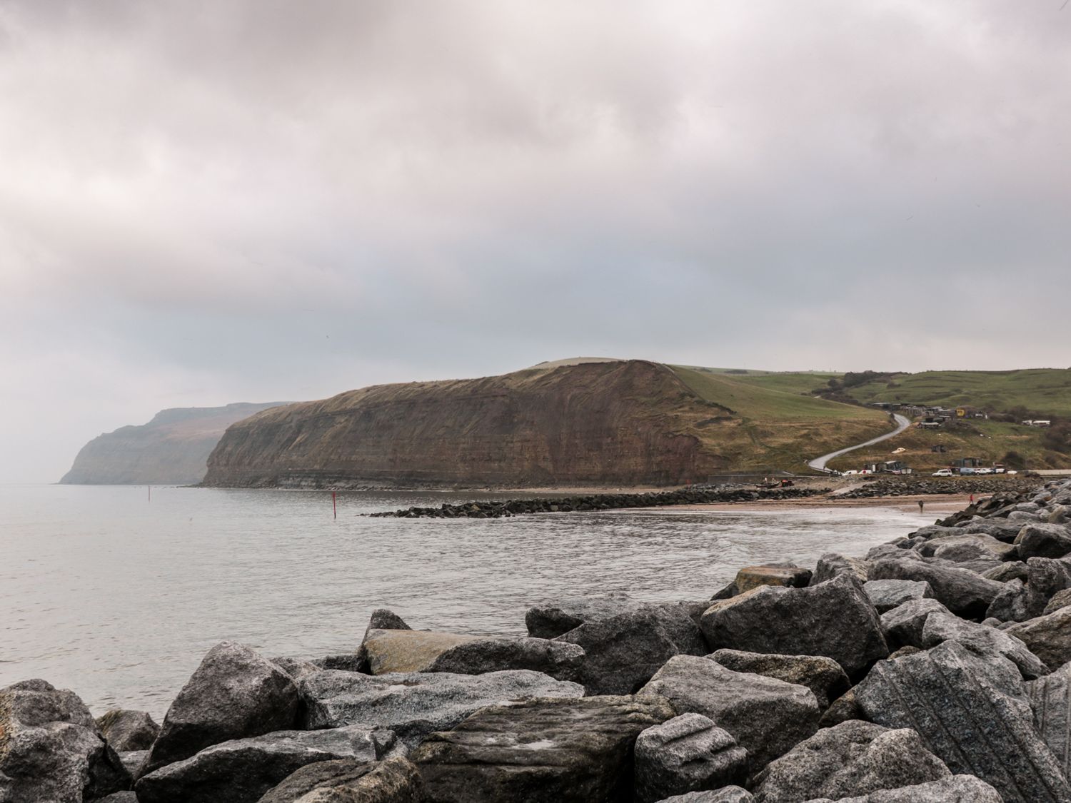 A rocky shoreline with cliffs in the background and a road leading to buildings at Lady Bird Retreat in Skinningrove