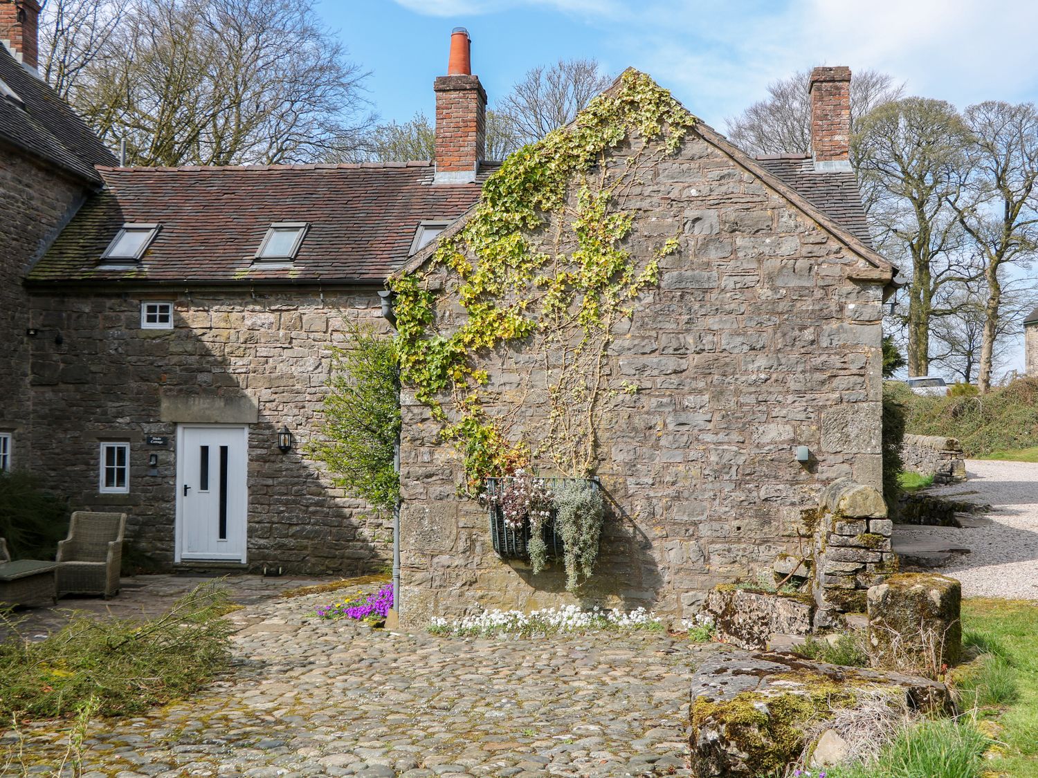 An exterior view of a stone cottage with a white door and a cobblestone pathway at Slade Cottage in Ilam