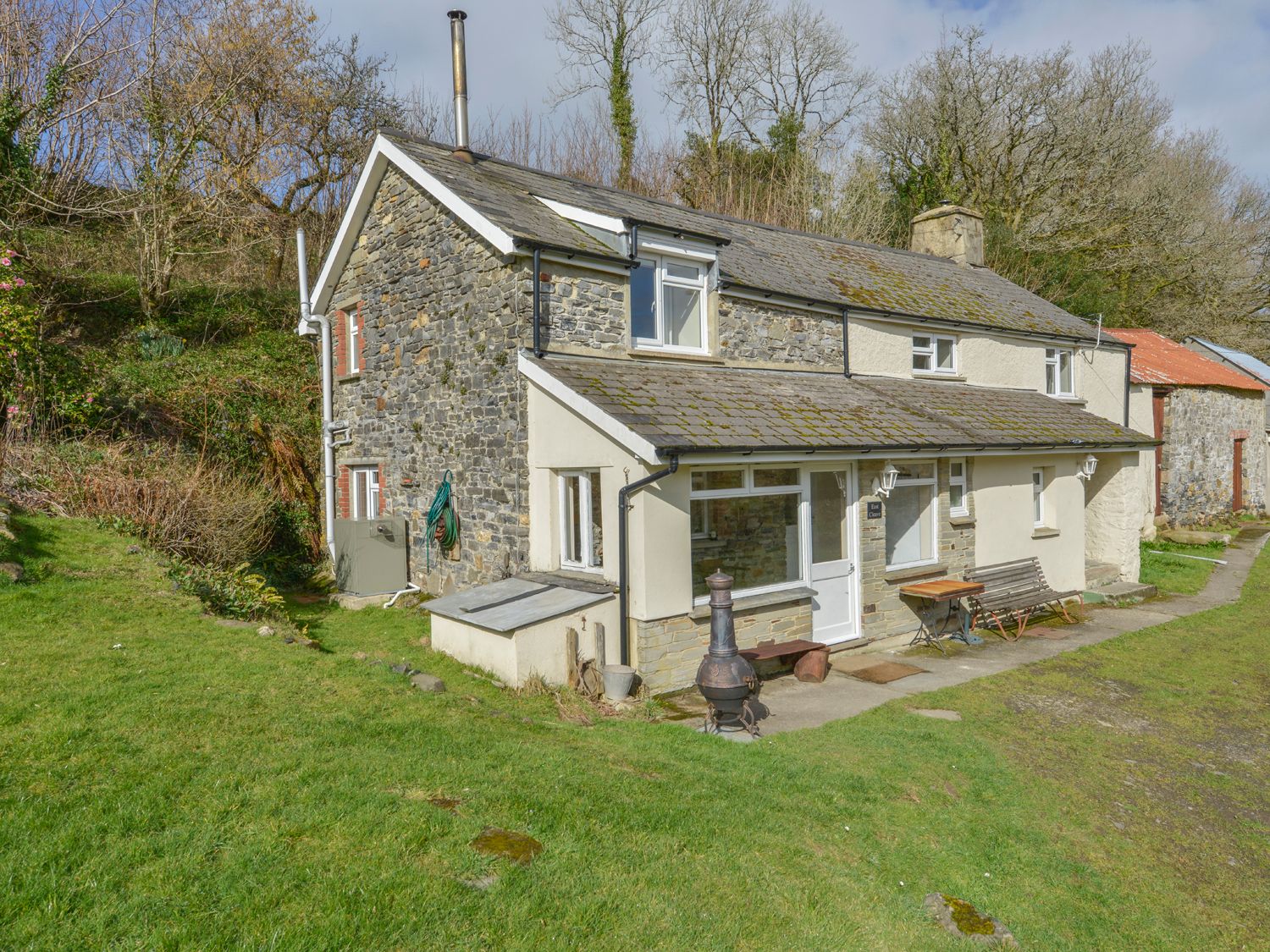 A stone and plaster house with a patio, bench, table, and lawn at East Cleave in Bridestowe