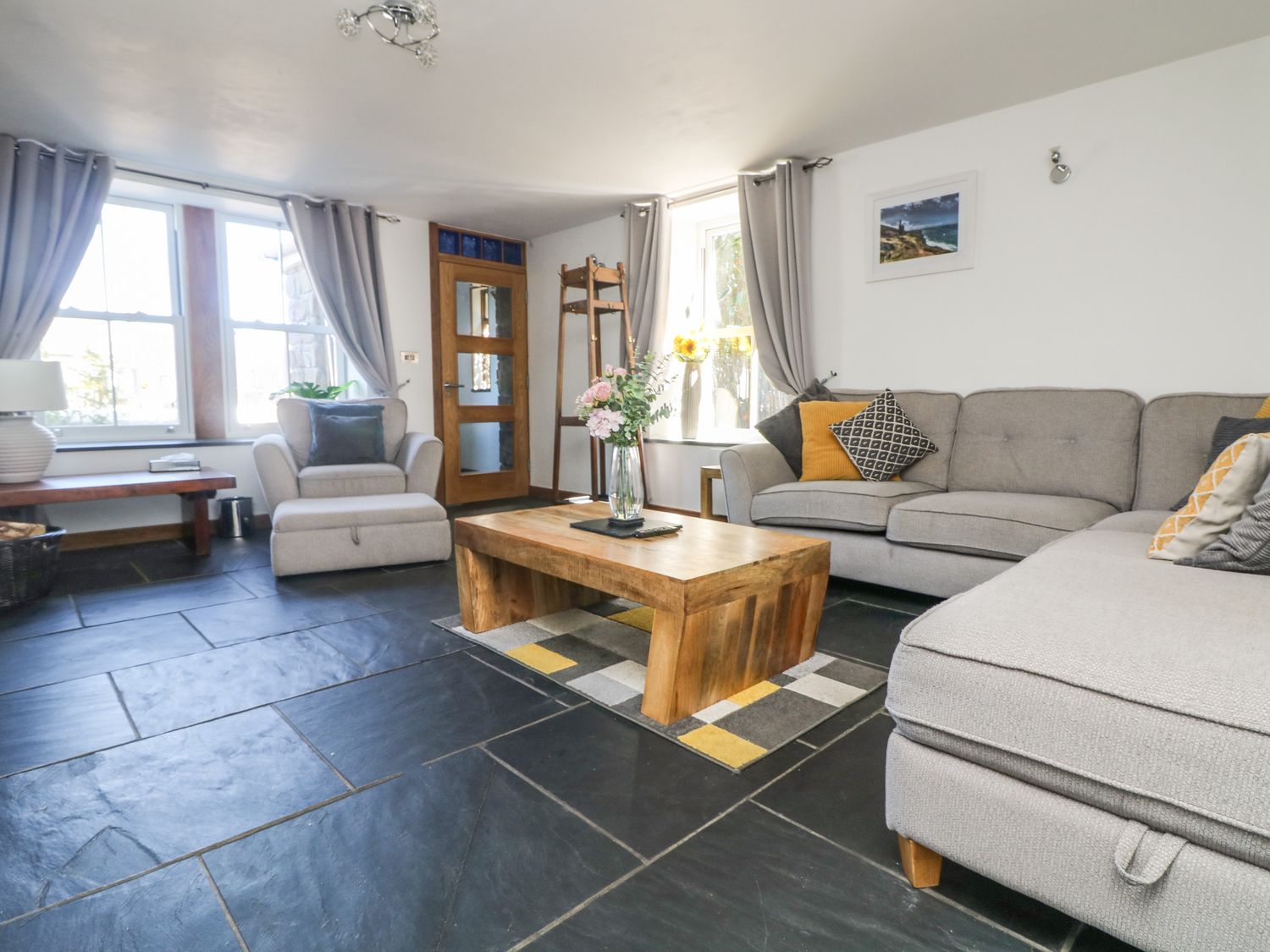 A living room with a sofa armchair wooden coffee table and a window at Miner's Rest in Troon near Camborne