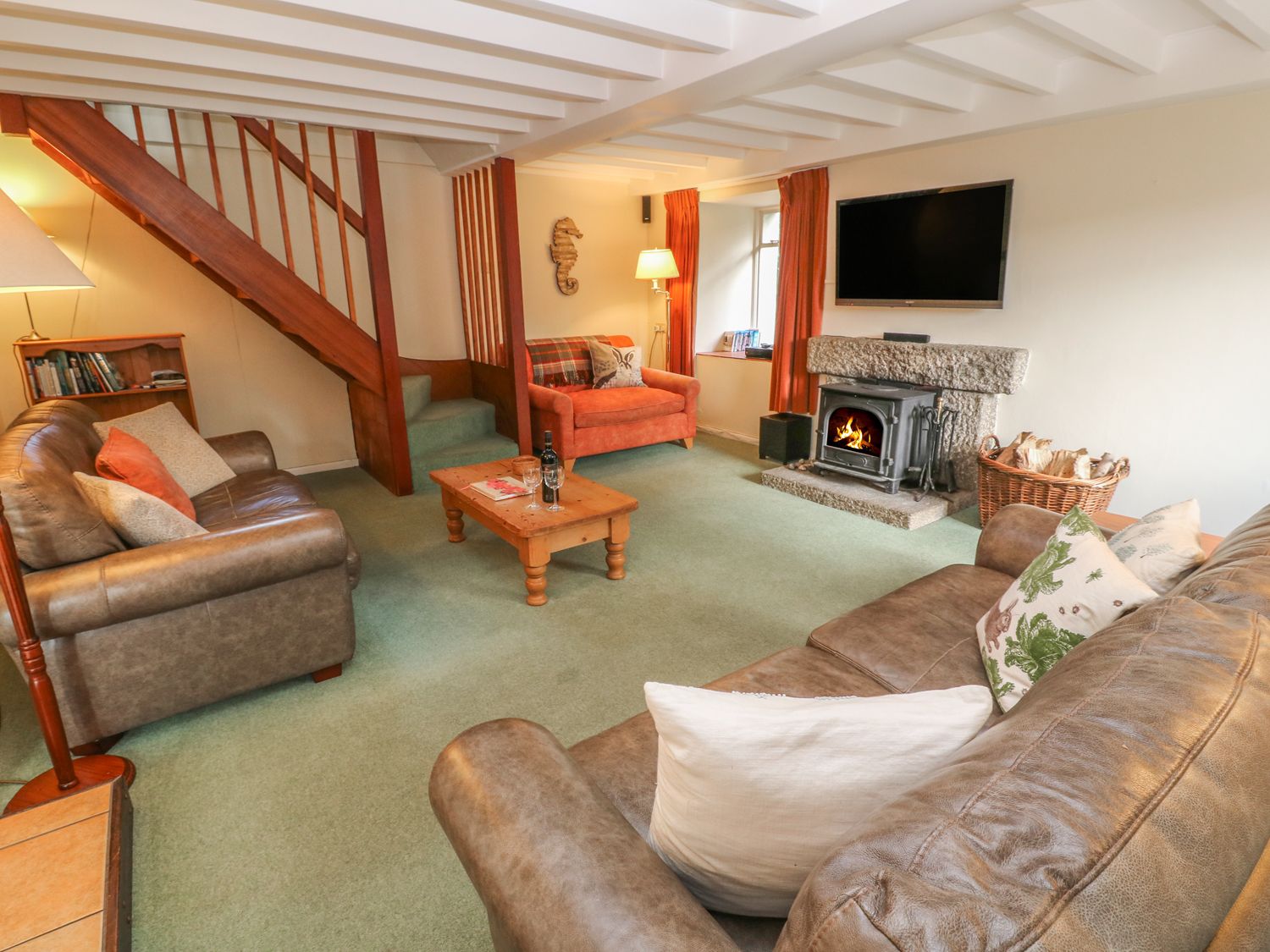 A living room with two leather sofas an armchair a wooden coffee table a fireplace with a fire and a wall-mounted television at Lampra Mill Cottage in Mullion