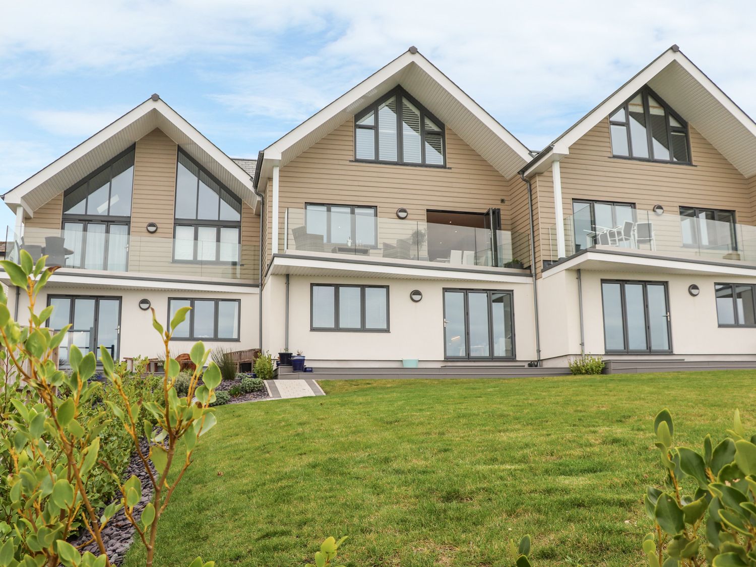 A row of modern houses with balconies and large windows overlooking a green lawn at Praa Waves in Praa Sands