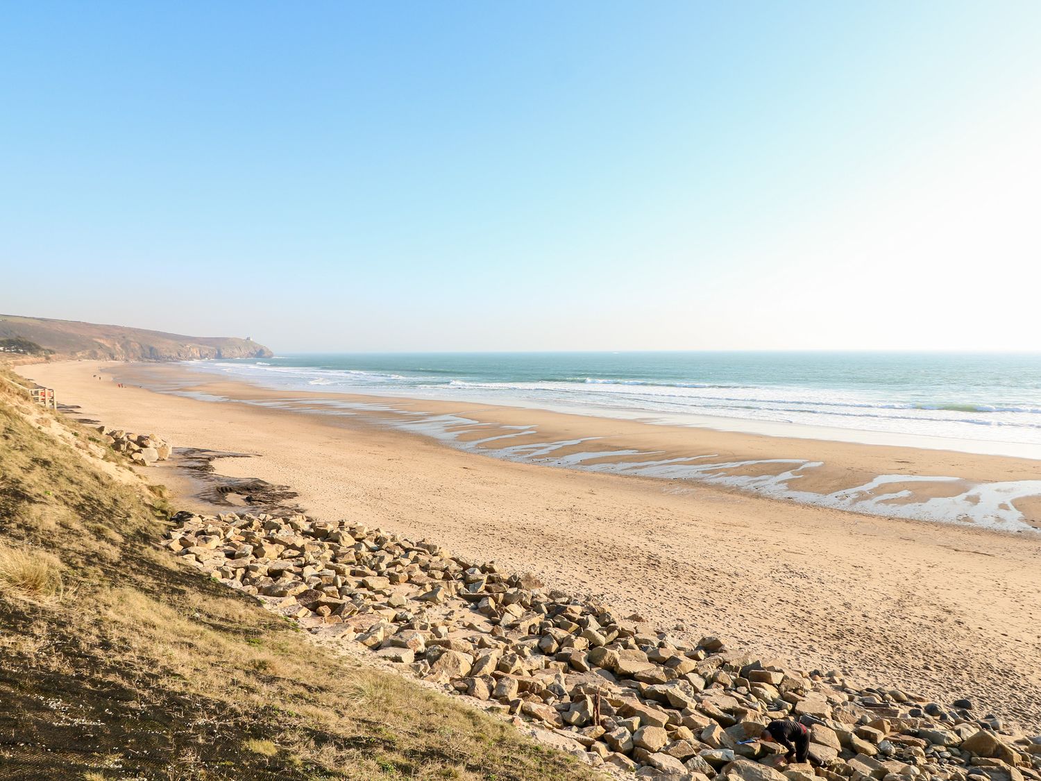 A sandy beach with waves rolling in rocks on the shore and cliffs in the distance at Praa Waves in Praa Sands