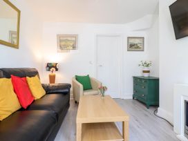 A living room with a black sofa with yellow and red cushions a beige armchair with a green cushion a wooden coffee table with flowers a green chest of drawers and a wall-mounted TV at 6 Smithfield Lane in Dolgellau