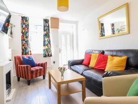 A living room with a black leather sofa with red and yellow cushions a striped armchair a wooden coffee table with flowers a fireplace and floral curtains at 6 Smithfield Lane in Dolgellau