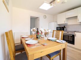 A kitchen with a wooden dining table set for four near white cabinets and appliances at 6 Smithfield Lane in Dolgellau