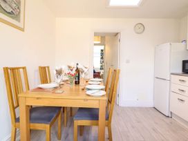 A dining area with a wooden table set with plates and glasses and wooden chairs next to a kitchen area with a refrigerator and microwave at 6 Smithfield Lane in Dolgellau