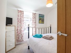 A bedroom with a metal bed, white bedding, folded towels, a chest of drawers with a TV, floral curtains, and a framed railway poster on the wall at 6 Smithfield Lane in Dolgellau
