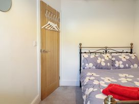 A bedroom with a bed with floral bedding and red towels on it and a wooden door with hangers at 6 Smithfield Lane in Dolgellau