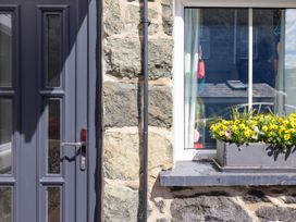 A stone wall with a gray door on the left and a window with a flower box containing yellow flowers on the right at 6 Smithfield Lane in Dolgellau