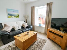 A living room with a black leather sofa and wooden coffee table a TV on a wooden stand and a window with beige curtains at Llewelyn House in Llandudno