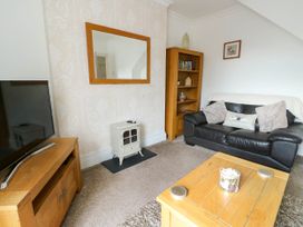 A living room with a black leather sofa wooden bookshelf wooden coffee table and a television at Llewelyn House in Llandudno