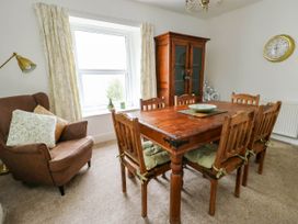 A dining room with a wooden table and six chairs a brown armchair a wooden cabinet and a window with curtains at Llewelyn House in Llandudno