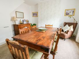 A dining room with a wooden table and chairs a sideboard with a lamp and statue an armchair with cushions and a floor lamp at Llewelyn House in Llandudno