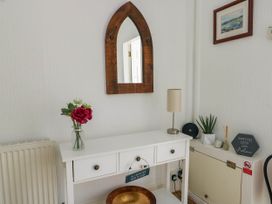 A white table with three drawers holding a flower vase lamp and decorations below a wooden framed mirror on a white wall at Llewelyn House in Llandudno