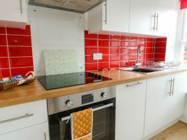 A kitchen with red tiled backsplash wooden countertop oven stovetop and white cabinets at Llewelyn House in Llandudno