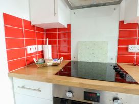 A kitchen countertop with an electric stove a basket with tea bags and paper towels against red tiled walls at Llewelyn House in Llandudno
