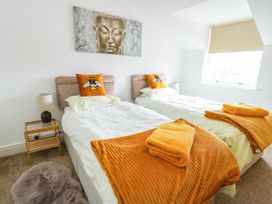 A bedroom with two single beds orange blankets and bee pillows a bedside table with a lamp and a window with a blind at Llewelyn House in Llandudno