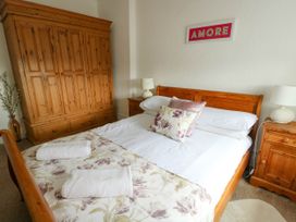 A bedroom with a wooden bed and wardrobe two bedside tables with lamps floral pillows and a framed print on the wall at Llewelyn House in Llandudno