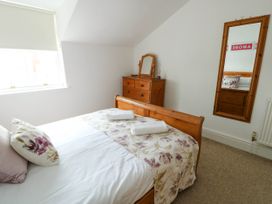 A bedroom with a wooden bed with floral bedding and pillows a wooden dresser with a mirror and a wall mirror at Llewelyn House in Llandudno
