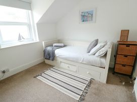 A bedroom with a white daybed with pillows and a blanket near a window and a striped rug on the floor at Llewelyn House in Llandudno
