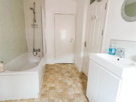 A bathroom with a bathtub shower combination a white sink with cabinet a door and a mirror at Llewelyn House in Llandudno