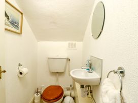 A small bathroom with a toilet with wooden seat a wall-mounted sink a round mirror a towel ring with a white towel a toilet paper holder and a framed picture on the wall at Llewelyn House in Llandudno