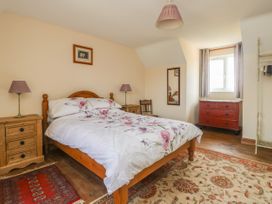 A bedroom with a wooden bed with floral bedding two bedside tables with lamps a red chest of drawers and a chair at Wayside Cottage in Pocklington