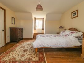 A bedroom with a wooden bed with floral bedding a chest of drawers a bedside table with a lamp and a patterned rug at Wayside Cottage in Pocklington
