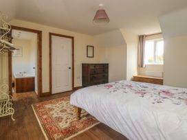 A bedroom with a bed covered in a floral duvet a wooden chest of drawers a window a rug and an open door leading to a bathroom at Wayside Cottage in Pocklington