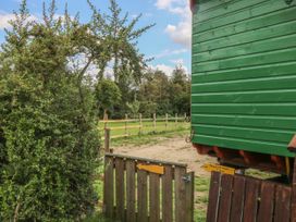 A wooden gate next to a green wooden structure with a fenced grassy area and trees in the background at Wayside Cottage in Pocklington